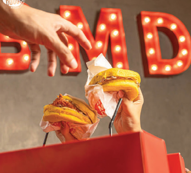 Hands holding burgers under lit BMD marquee letters