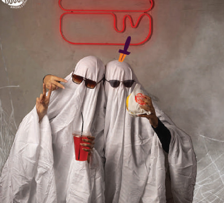 Ghost-costumed pair with a burger and drink under a neon burger sign