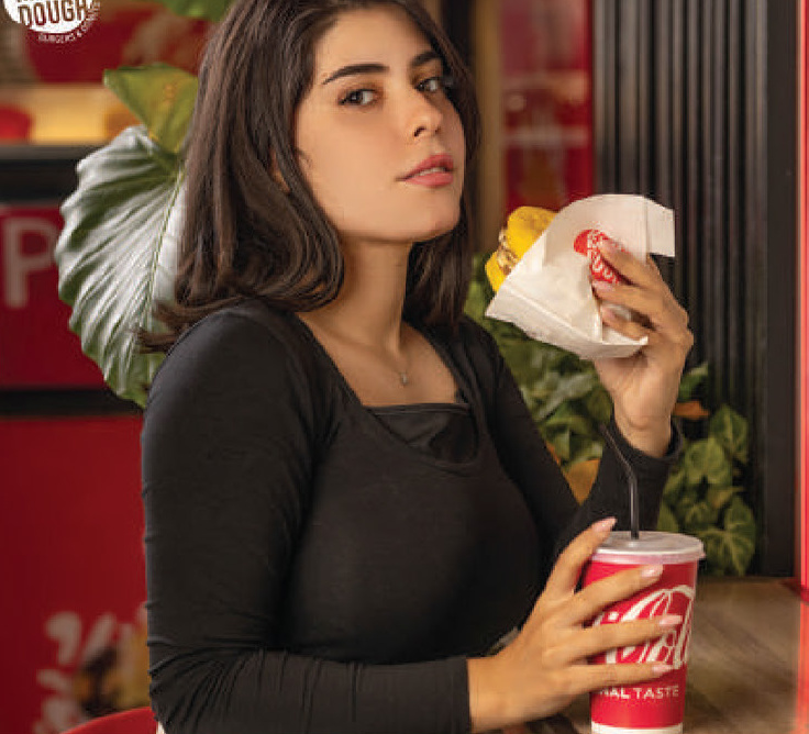 Woman holding a wrapped burger and a branded cup at the restaurant