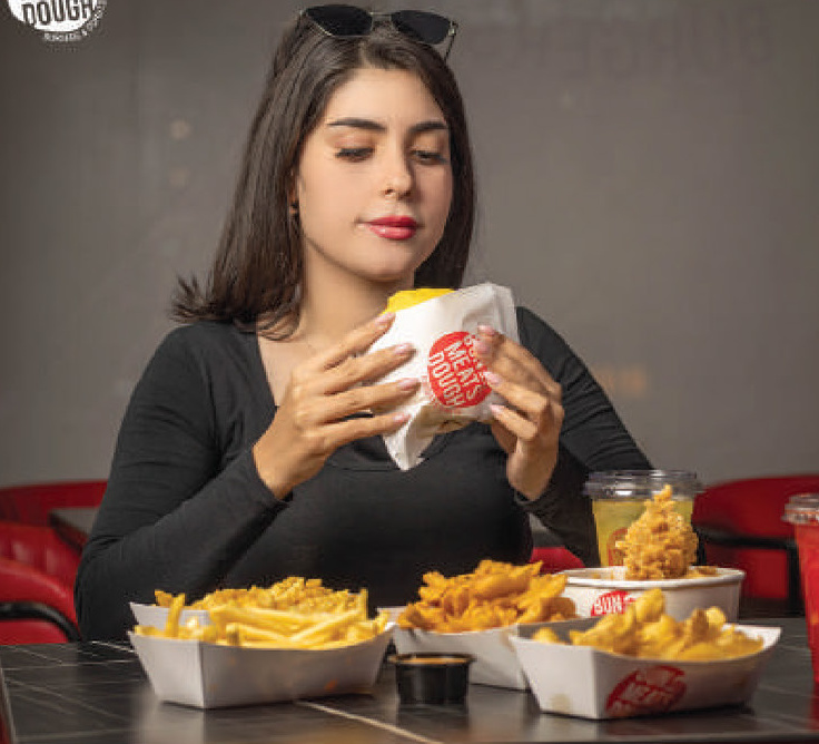 Woman unwrapping a burger beside fries and chicken boxes