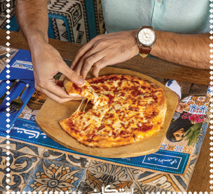 Hands lifting a slice of cheese pizza on a wooden board